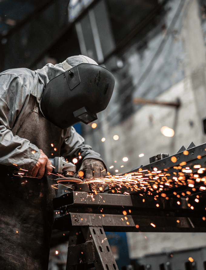 Worker in protective gear using a grinder, creating sparks in a workshop.