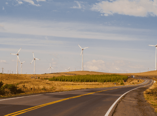 Road passing through a landscape with wind turbines in the background.