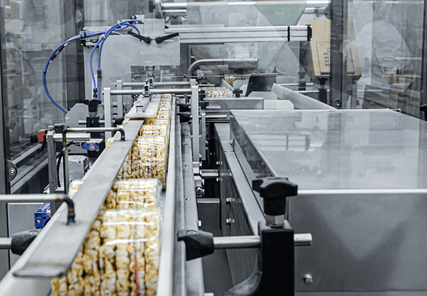 Automated packaging line with wrapped food products moving along a conveyor belt in a factory setting.