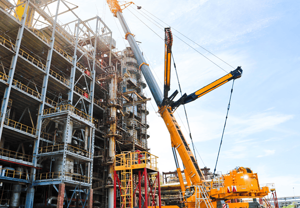 A yellow construction crane lifting materials at a building site with scaffolding and unfinished structures in the background.