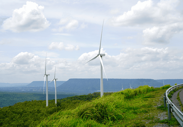 Wind turbines on a grassy hill with a mountainous landscape in the background.