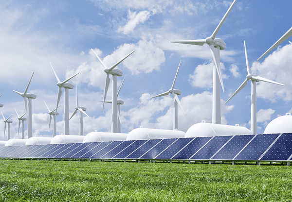 Wind turbines and solar panels on a grassy field under a partly cloudy sky.