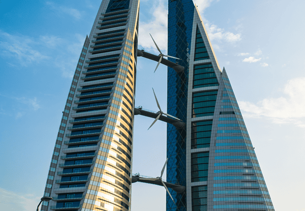 Two modern skyscrapers with integrated wind turbines between them against a blue sky.