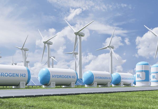 Wind turbines and hydrogen storage tanks in a green field under a partly cloudy sky.