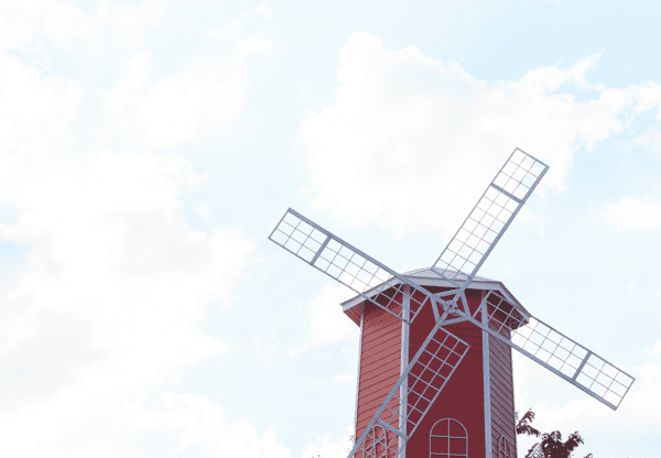 Red windmill with white blades against a partly cloudy sky.