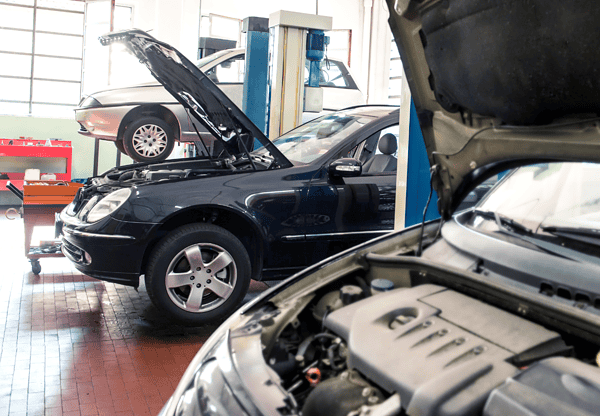 A garage with two cars being repaired, one with its hood open and the other partially visible in the foreground.