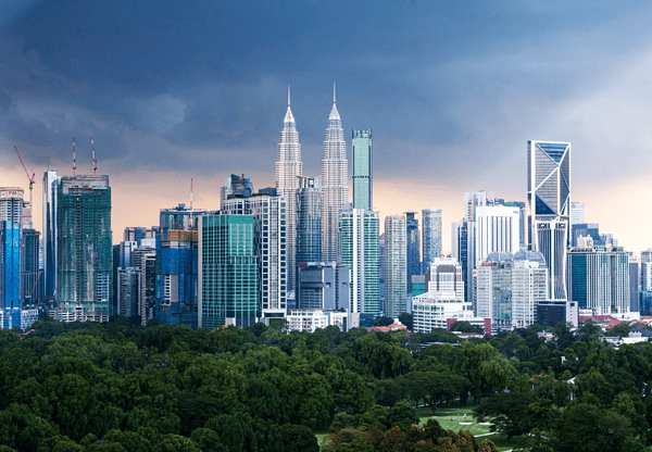 City skyline with tall skyscrapers and a park in the foreground under a cloudy sky.