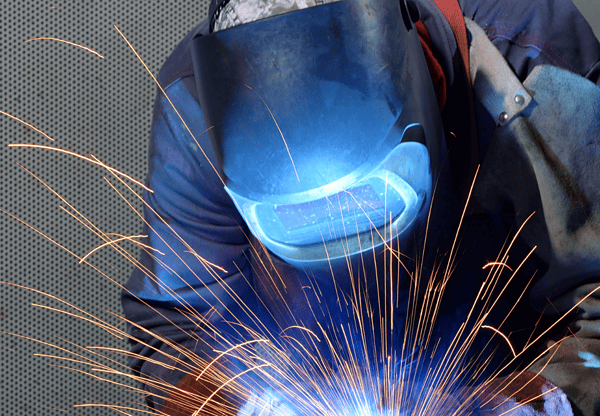 Welder in protective gear working with sparks flying.