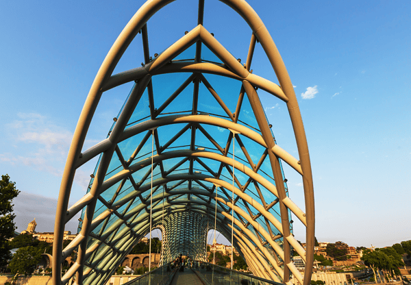 Modern glass and steel pedestrian bridge with an arched design.