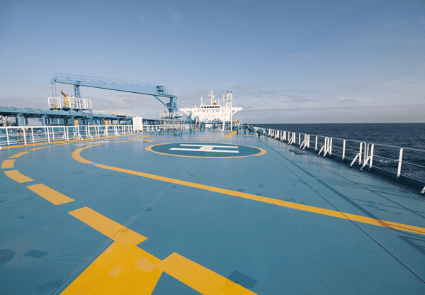 Helipad on the deck of a ship with a blue crane in the background.