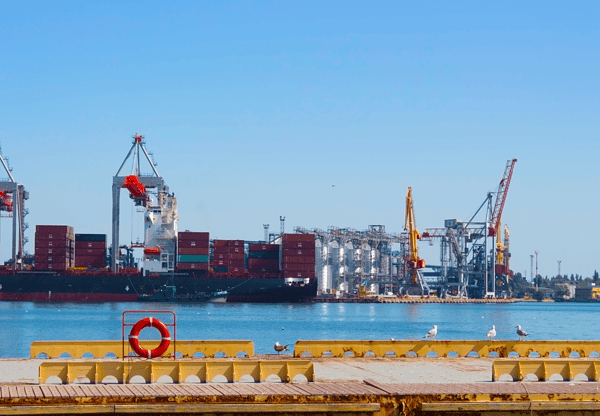 A container ship docked at a port with cranes and industrial structures in the background.