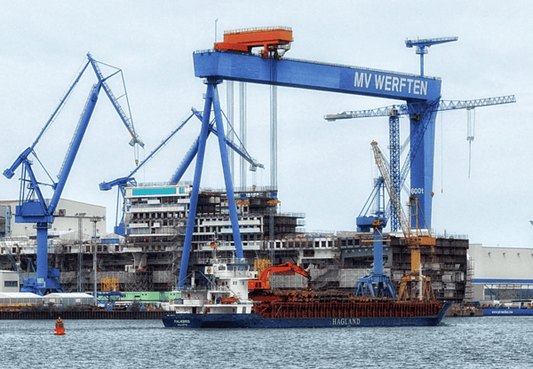 Shipyard with large blue cranes and a cargo ship docked.