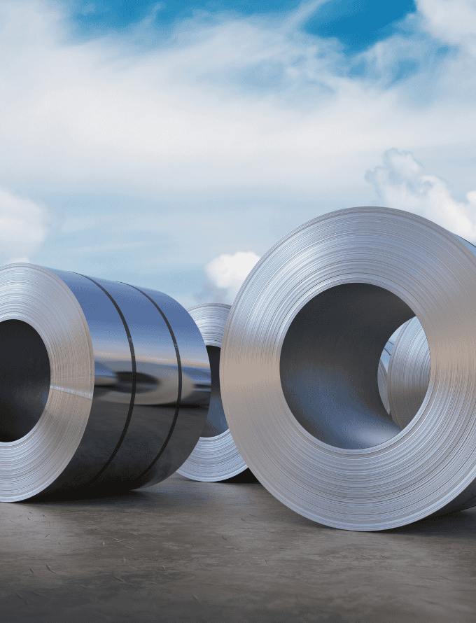 Large rolls of steel sheets on an outdoor surface with a cloudy sky background.