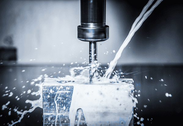 Close-up of a CNC machine cutting a metal piece with coolant spraying.