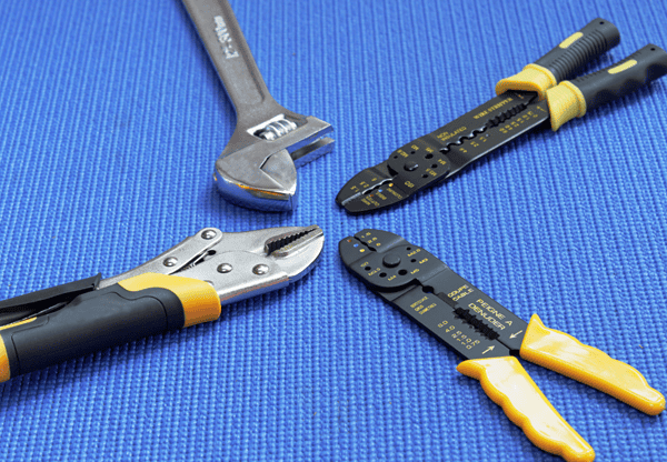 Various hand tools including an adjustable wrench, wire strippers, and pliers on a blue background.