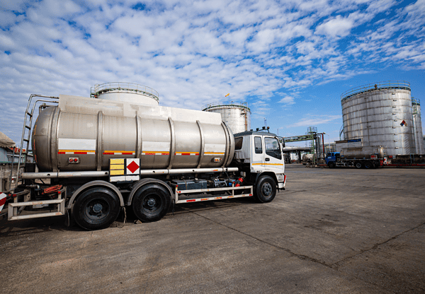 Tanker truck parked in an industrial facility with large storage tanks in the background.