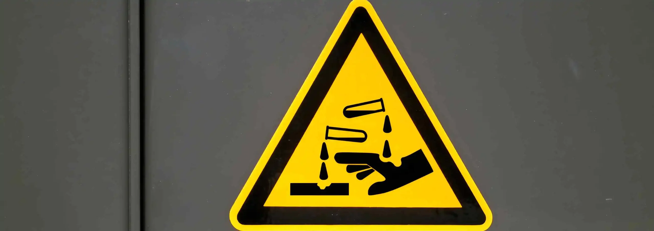 A warning sign indicating a chemical hazard, relevant to the handling and processing of plain carbon steel bars.