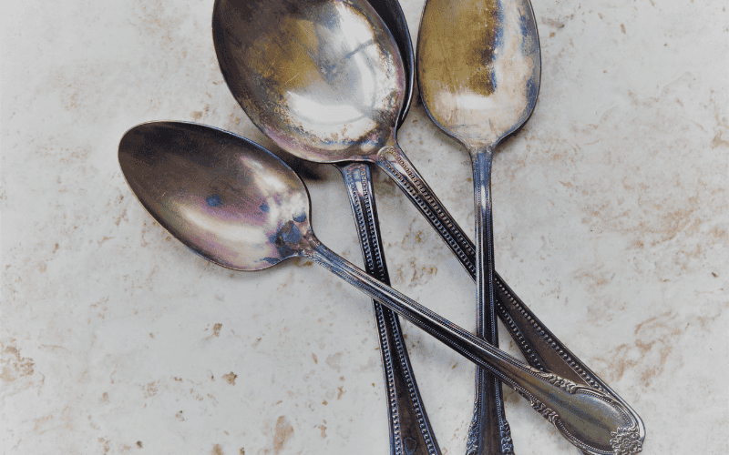 Tarnished stainless steel spoons on a marble surface.