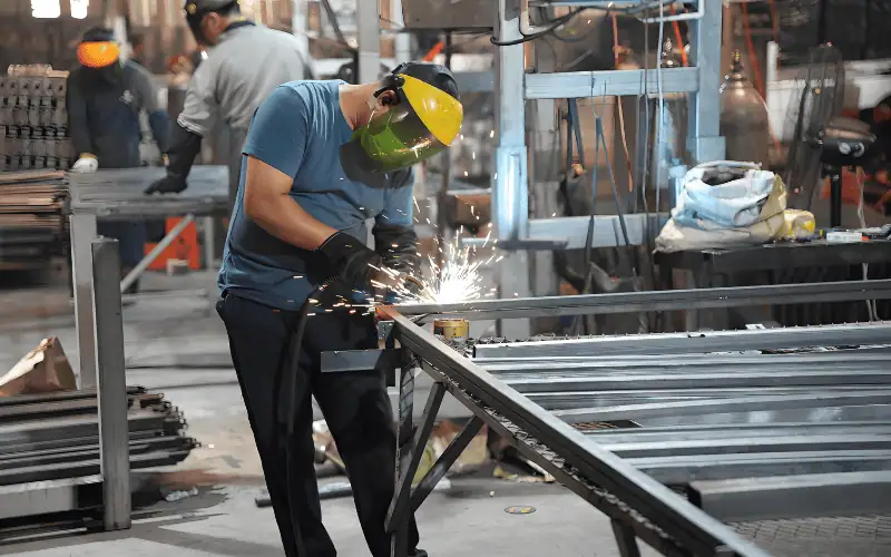 A welder wearing protective gear works on metal fabrication in an industrial setting.