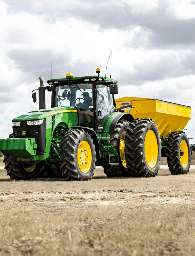 Ein grüner Traktor mit einem gelben Anhänger auf einem Feld, der die Verwendung von legiertem Stabstahl in schweren Landmaschinen veranschaulicht.