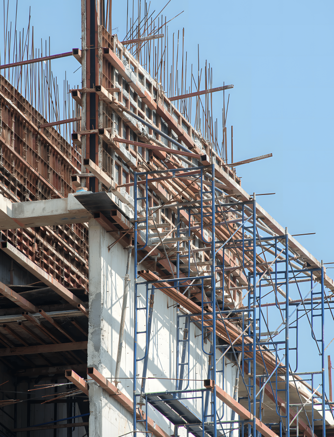 Baustelle mit Gerüsten und vorstehenden Stahlstangen unter blauem Himmel.