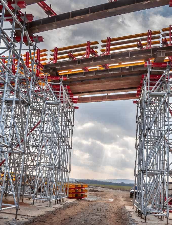 Construction site with scaffolding supporting a large bridge structure under construction.