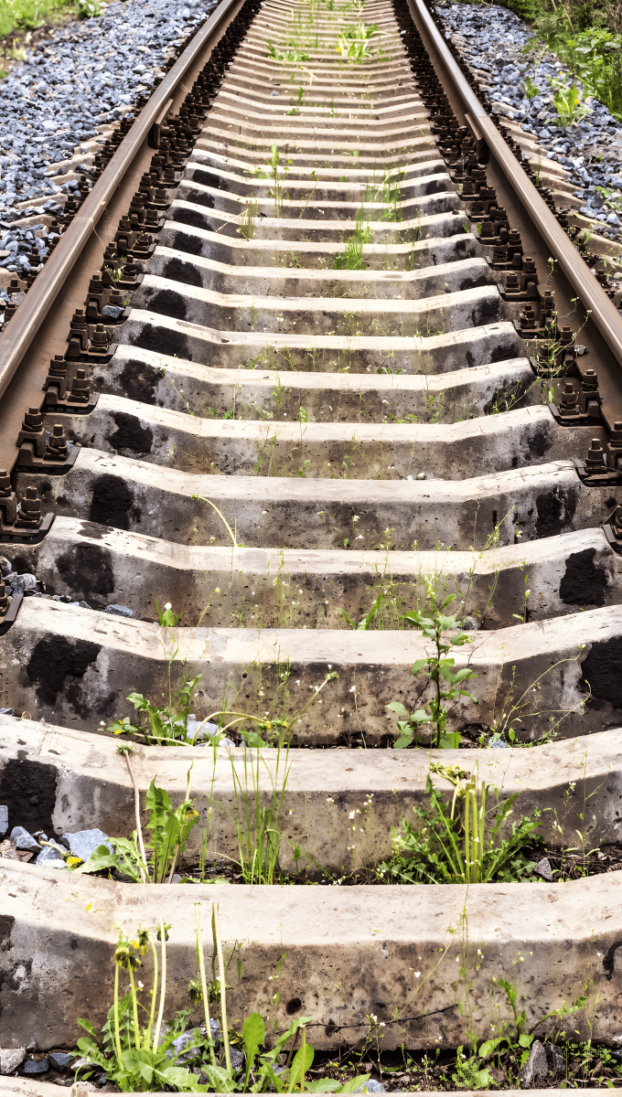 コンクリート製の枕木が敷かれた線路のクローズアップ。線路に使用される鋼鉄と、鉄道車体に使用される鋼鉄の耐久性が強調されている。