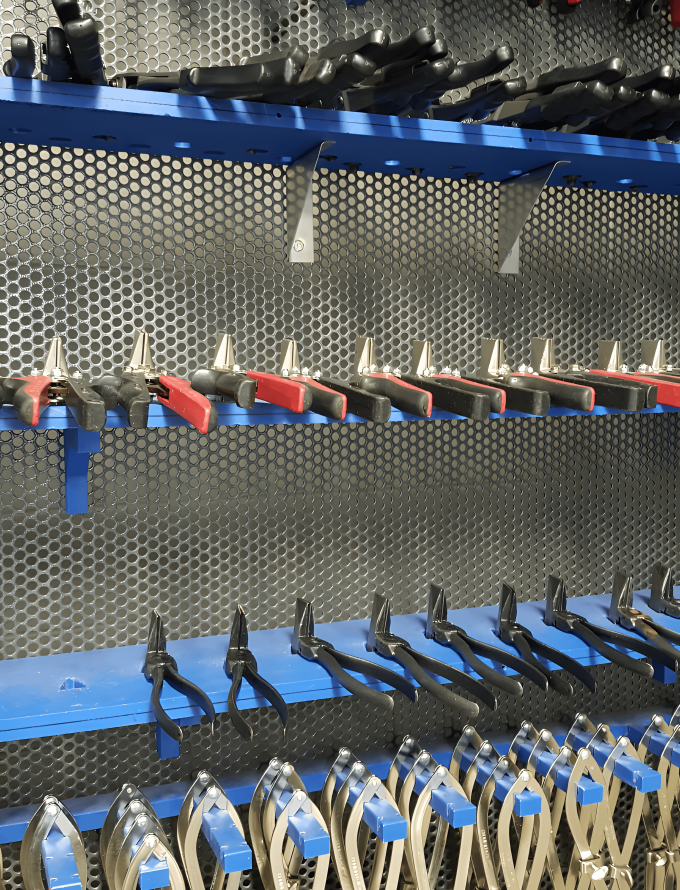 Various pliers and hand tools, made from tool steel bars, organized on shelves in a workshop.