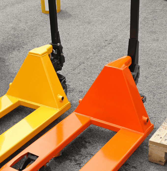 Two orange and yellow pallet jacks on a concrete surface.