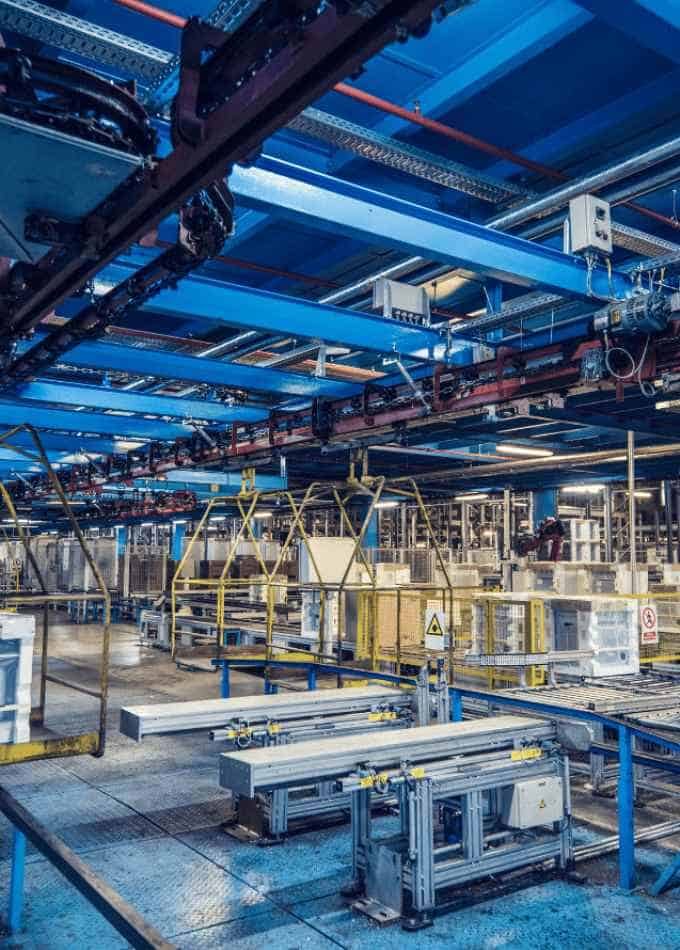 Interior of an industrial manufacturing facility with blue steel beams, overhead conveyors, and complex machinery setups.