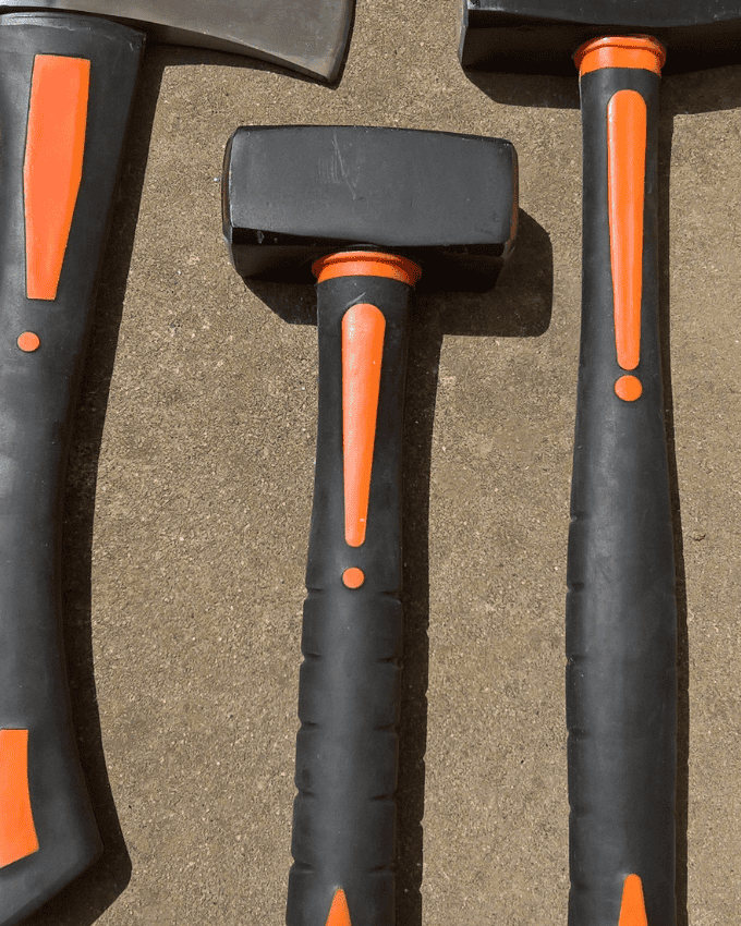 Three black and orange hammers with rubber handles on a concrete surface.