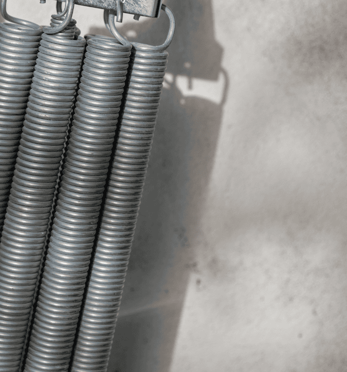 Close-up of metal springs hanging vertically against a concrete wall, highlighting their coiled structure.