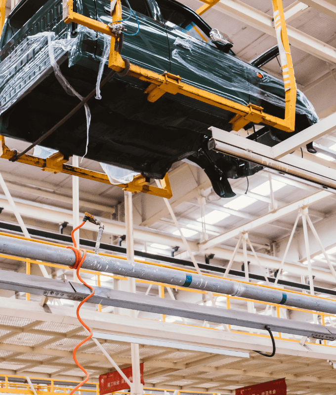 High strength steel bar used in automotive manufacturing, suspended on an overhead conveyor system in a factory setting.