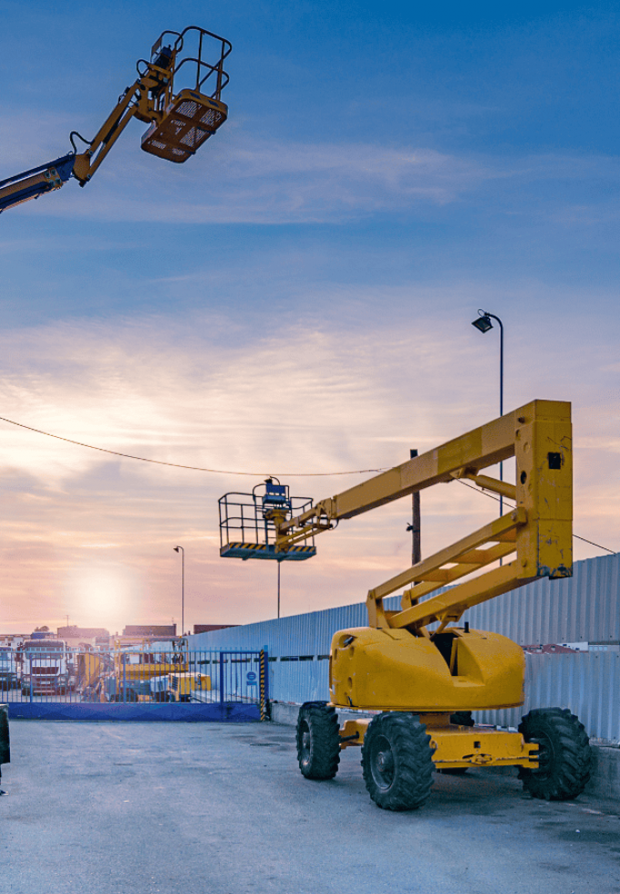 Construction site with yellow mobile elevating work platforms at sunset.