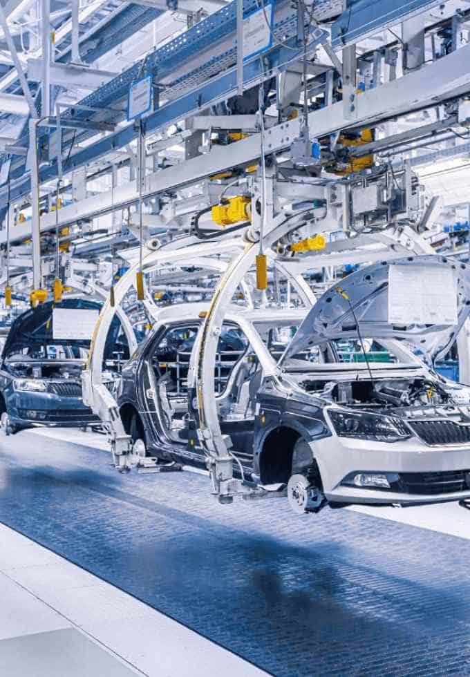 Automated assembly line with robotic arms assembling vehicles in a car manufacturing plant.