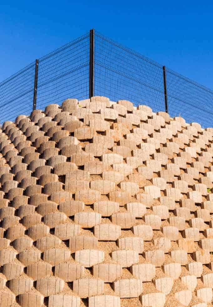 Large stack of wooden pallets with a fence on top, under a clear blue sky.