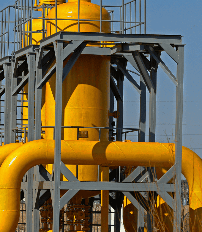 Industrial structure with large yellow pipes and cylindrical tanks, supported by a metal frame.