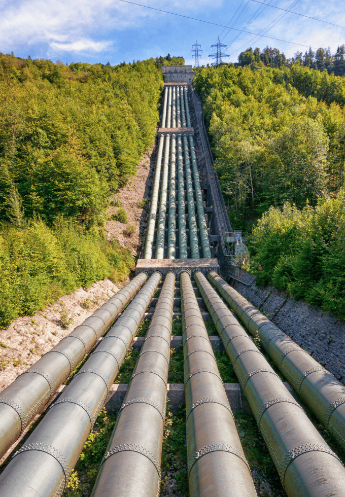 View of large industrial pipelines running down a forested hillside.