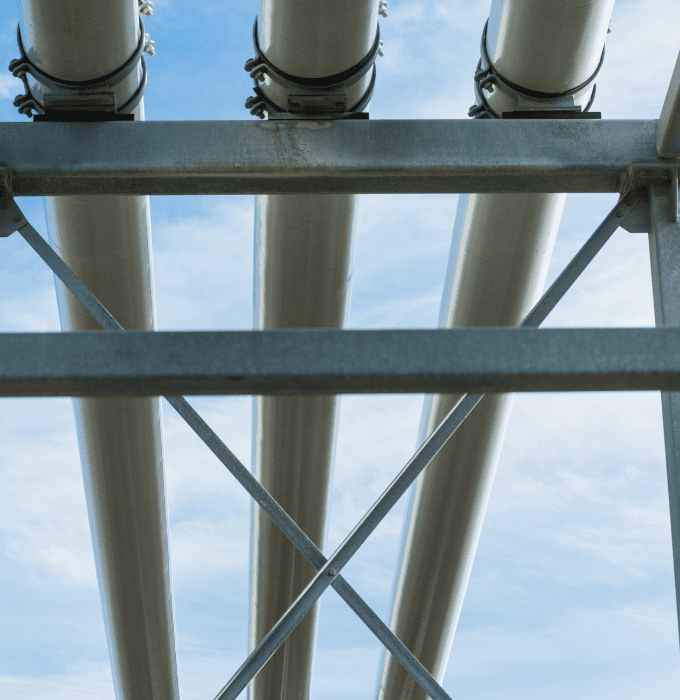 View from below of pipelines supported by a metal framework against a blue sky.