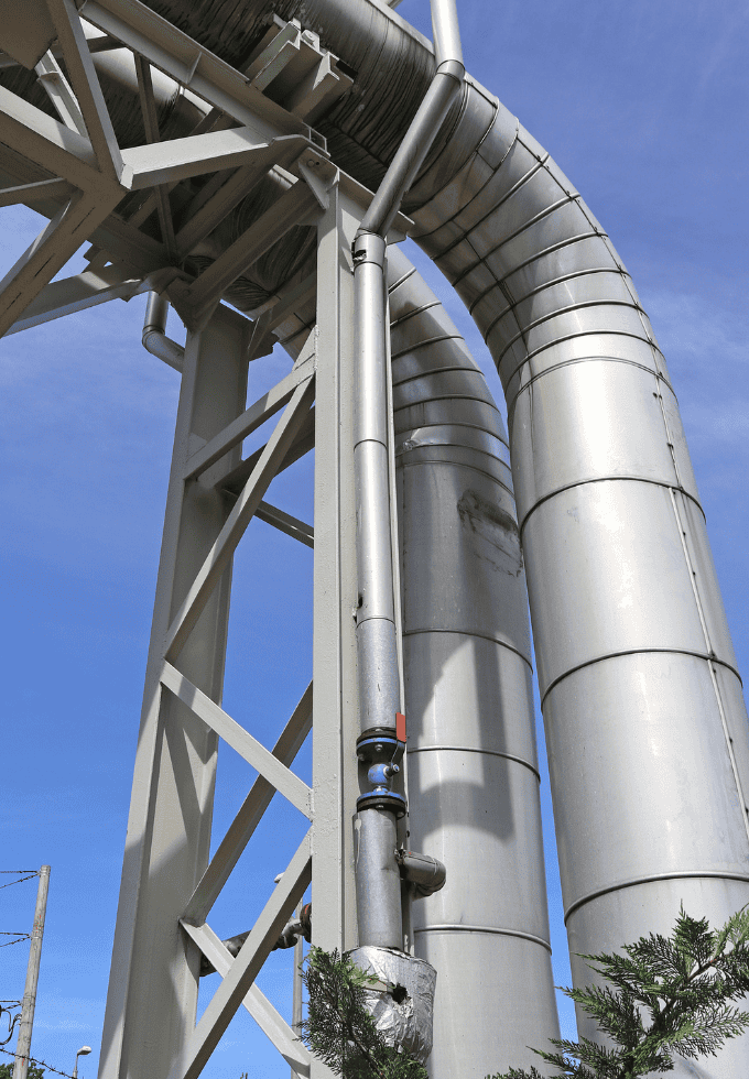 View from below of large curved industrial pipes supported by a metal structure.