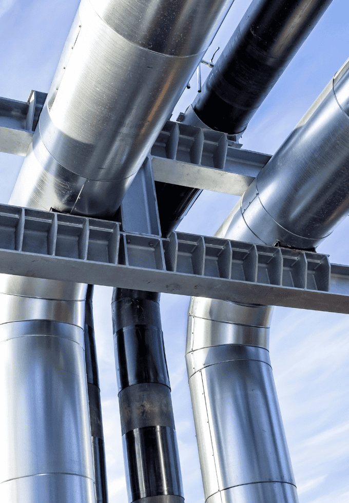 View from below of large industrial pipes supported by a metal framework against a blue sky.