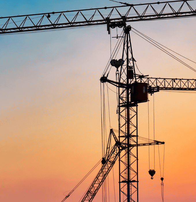 Construction cranes at a building site during sunset.