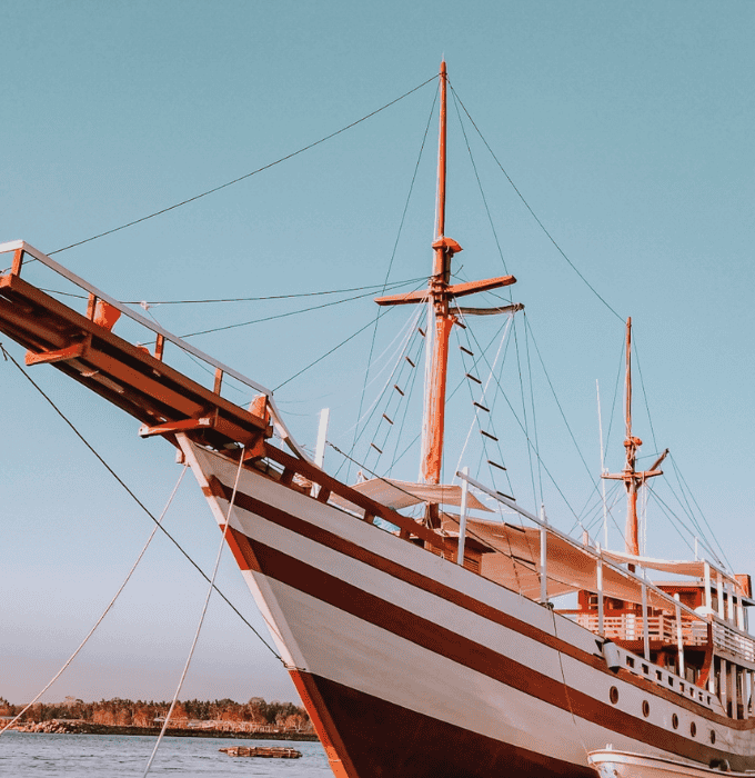 Sailing ship with tall masts docked in calm waters.