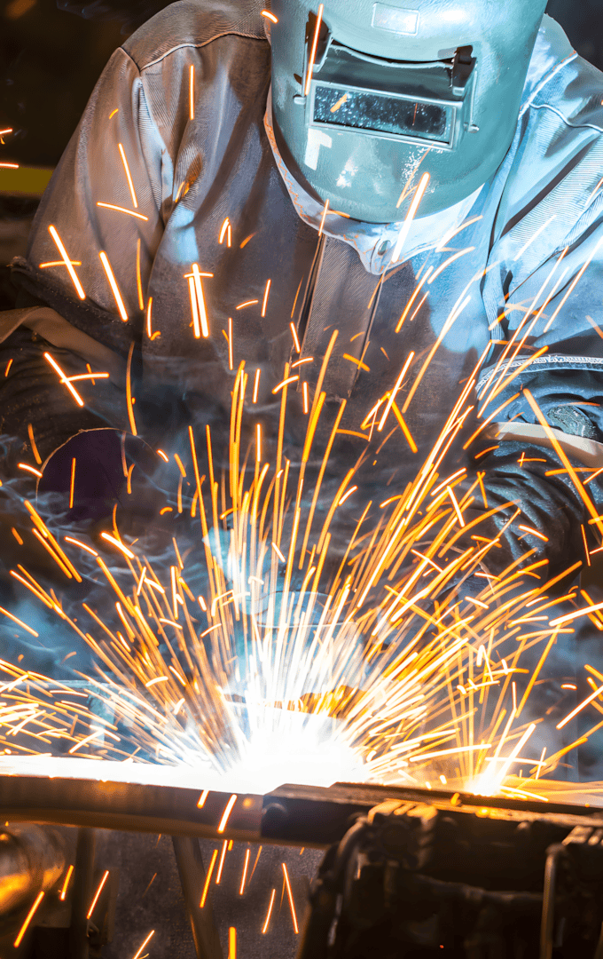 Welder working on a steel bar, creating bright sparks, showcasing the strength and versatility of steel in construction and manufacturing.