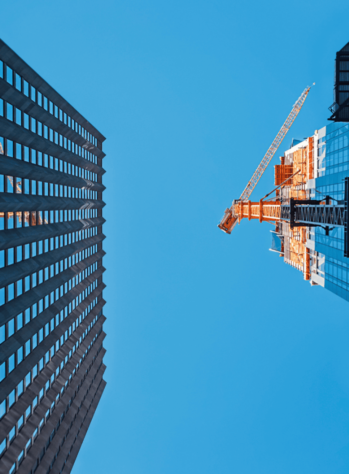 Looking up at a skyscraper and a construction crane against a clear blue sky.