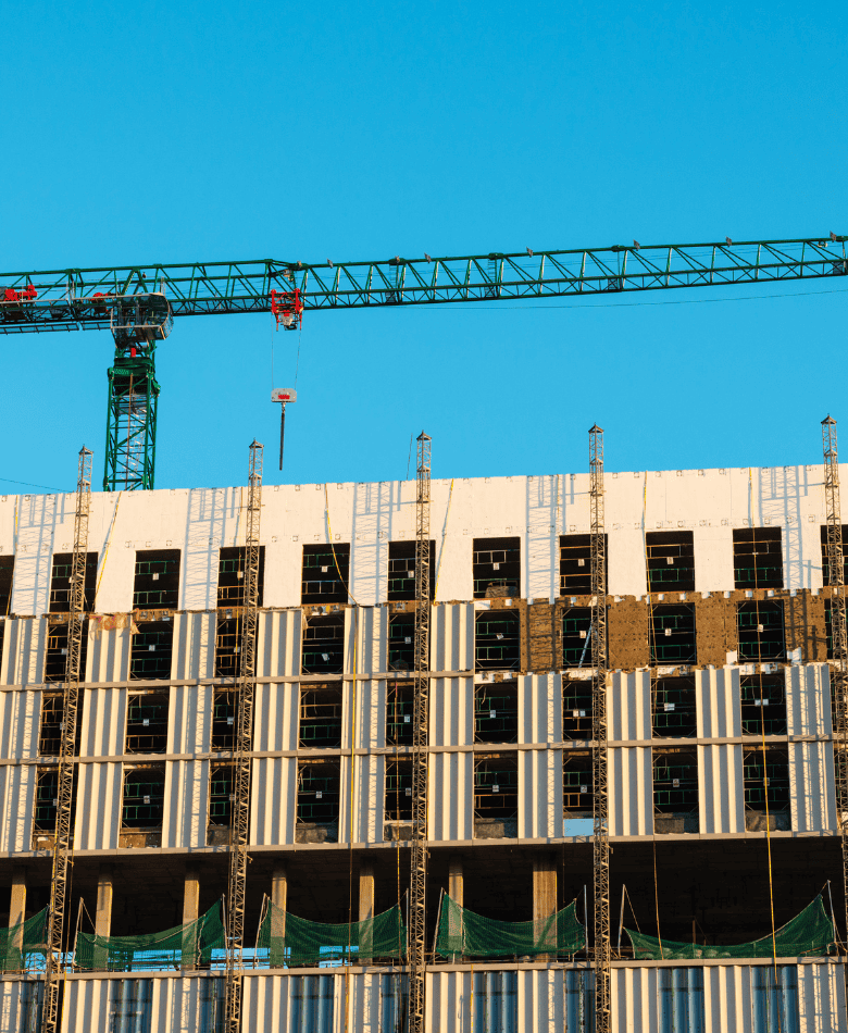 Building under construction with scaffolding and a green crane against a clear blue sky.