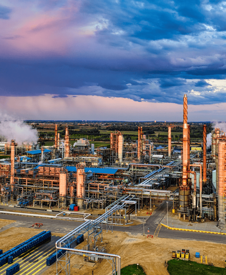 Industrial refinery complex with smokestacks and pipelines under a dramatic sky.