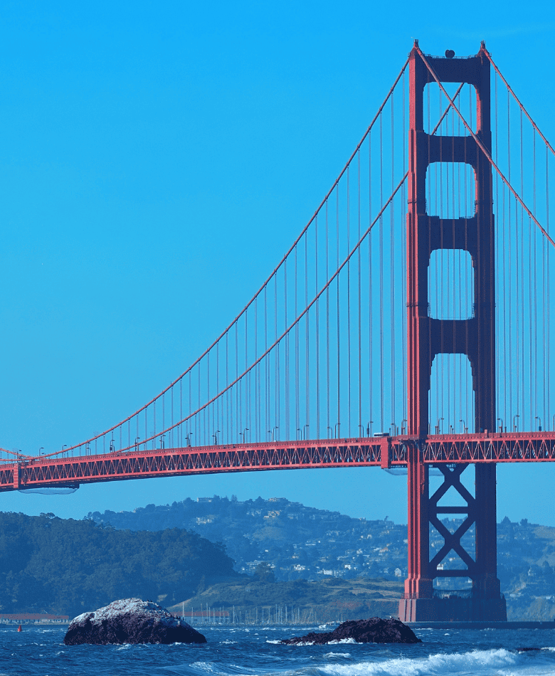 The Golden Gate Bridge with a clear blue sky and water in the foreground.